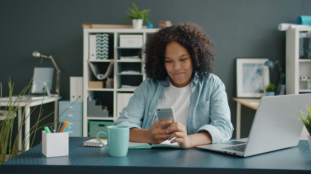 Femme consultant son téléphone devant son portable, à la maison